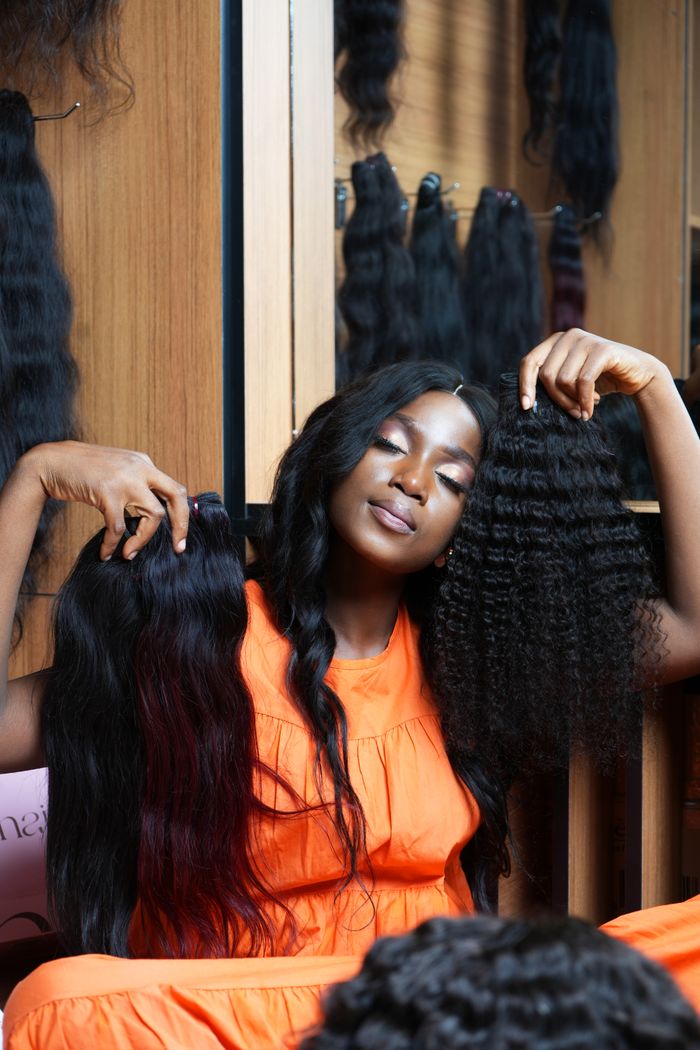 A fashionable woman in Accra displays two types of hair extensions with closed eyes.